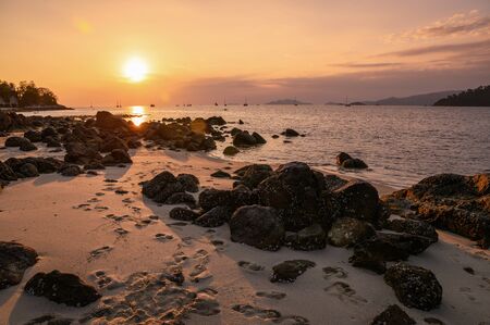 Rocks on coastline in tropical sea at sunsetの写真素材