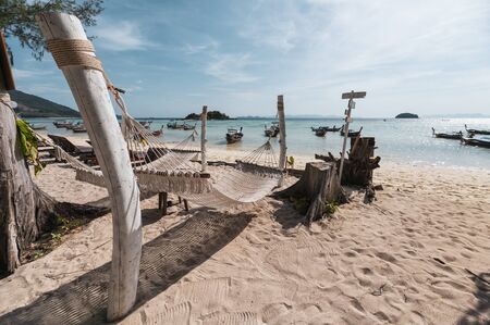 Rope cradle swing hanging on wood on the beach with wooden boat in tropical sea at morningの写真素材