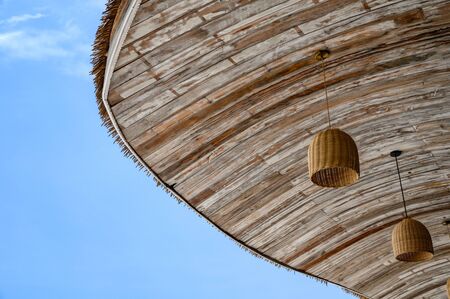 Wooden thatch roof with lamp hanging and blue skyの写真素材