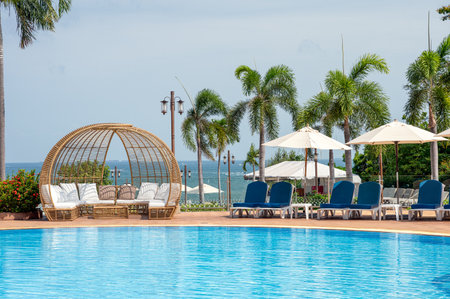 Pattaya, Thailand - May 26 2019 : Blue sunbeds with parasol with modern wooden chair on swimming pool in tropical seaのeditorial素材