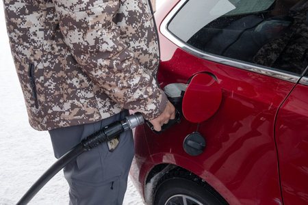 Man holding fuel pump nozzle with filling benzine oil in red car on winter in self-service petrol...