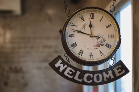 Vintage clock with roman number and welcome label hanging on ceiling