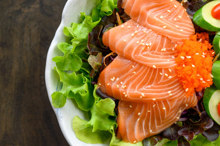 Slices of raw Salmon sashimi with vegetable in ceramic bowl on wooden table