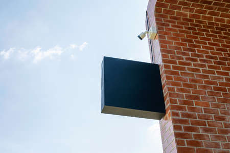 Empty shop signage with CCTV security camera hanging on brick wall and blue skyの写真素材