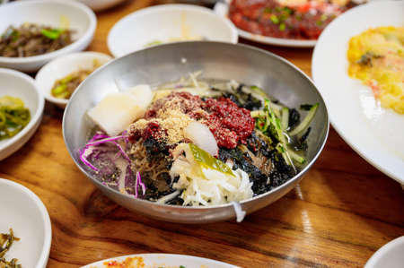 Cold noodle with vegetables, tofu, seaweed, sauce kimchi in zinc bowl on dining tableの写真素材