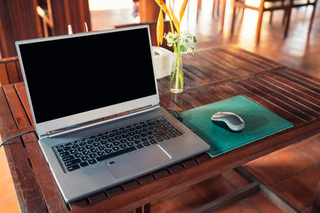 Modern laptop with wireless mouse and flower vase on wooden tableの写真素材