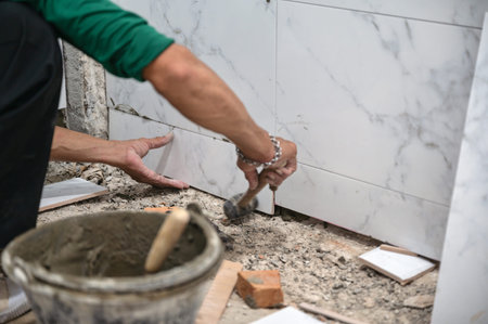 Male tiler using trowel laying marble tile with cement in bathroom. Housing development, Interior...