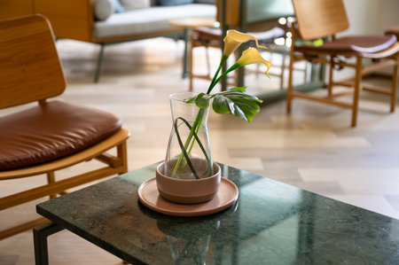 Beauty yellow flower with green leaves in glass vase on the table in living roomの写真素材
