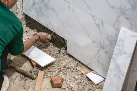 Male tiler using trowel laying marble tile with cement in bathroom. Housing development, Interior improvement renovationの写真素材