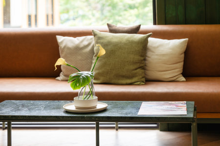 Beauty yellow flower with green leaves in glass vase on the table in living roomの写真素材