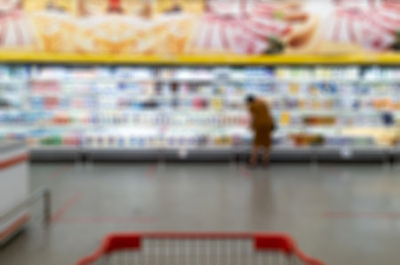 Shopping cart on blurred of consumer products on lighted shelves at supermarketの写真素材