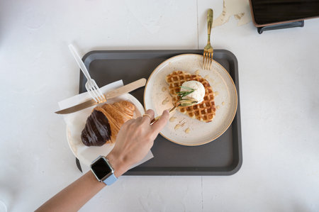 Top view of Hand using spoon scooping ice cream waffle and croissant on white table in cafeの写真素材