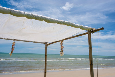 Seashell souvenir hanging decoration on wooden gazebo with tropical beach on sunny dayの写真素材