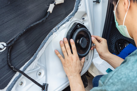 Mechanic man installing speaker on vehicle door part in workshop garageの写真素材