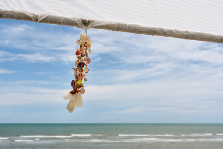 Seashell souvenir hanging decoration on wooden gazebo with tropical beach on sunny day