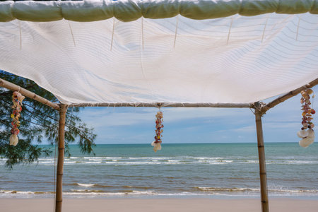 Seashell souvenir hanging decoration on wooden gazebo with tropical beach on sunny dayの写真素材