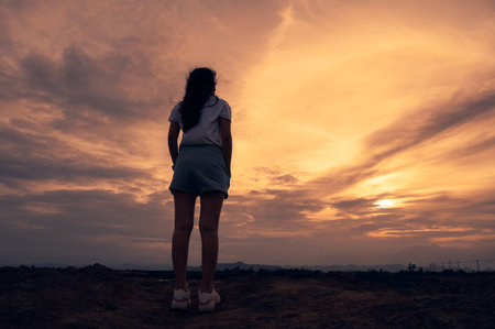 Back of silhouette confident asian woman standing and looking at colorful sunset skyの写真素材