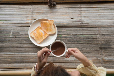 Female hand stirring hot cocoa drink in white cup on bamboo table in the morning. Top viewの写真素材