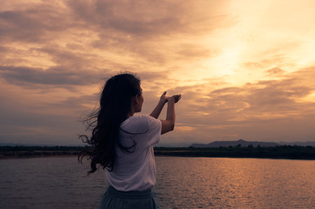 Young woman standing outstretched hands praying for blessing with sunset sky. Religion conceptの写真素材
