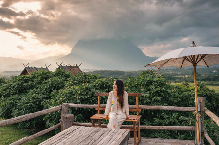 Young asian woman sitting on terrace and mountain view of Doi Luang Chiang Dao in the sunset at Chiang Mai, Thailandの写真素材