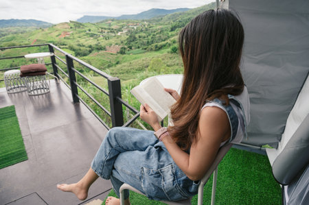 Back of asian woman sitting and reading a book on terrace among the nature in vacationの写真素材