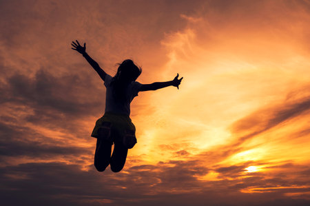 Silhouette successful young woman jumping outstretched hands in colorful sunset skyの写真素材
