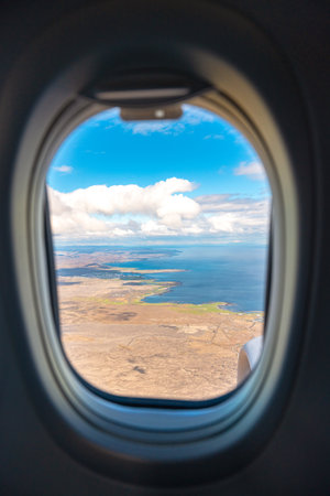 Airplane window frame view flying over land and ocean on sunny day. Travel and transportation conceptの写真素材
