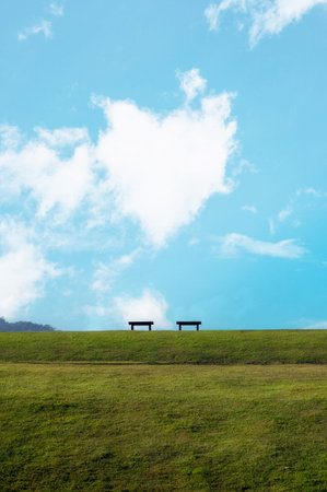 Two seat on green hill with heart shaped cloud in parkland on sunny day. No people tranquility and...