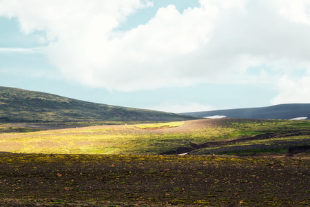 Weathered rugged moss hill mountain with sunlight and blue sky on summer in Icelandic highlands at...