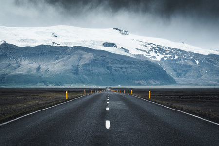 Dramatic straight asphalt road with storm over mountain on gloomy day in Iceland