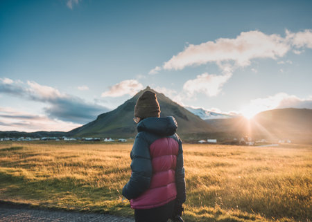 Tourist woman in winter jacket walking through Stapafell mountain and sunlight shining in the sunset at Arnarstapi village, Icelandの写真素材