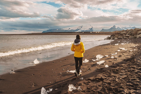 Young asian woman in yellow jacket walking on Diamond beach with iceberg melting in summer at Icelandの写真素材