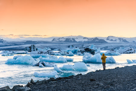 Tourist man in down jacket enjoying with iceberg and ice breaking in the sunset at Jokulsarlon glacier lagoon, Vatnajokull national park, Icelandの写真素材