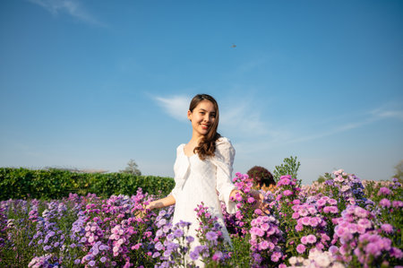 Beautiful young asian woman in white dress enjoying margaret flower blooming in garden on sunnyの写真素材
