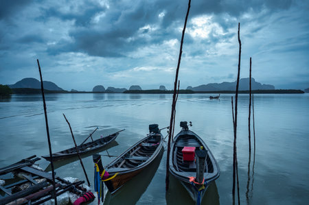 Traditional wooden fishing boat parked by the sea with moody sky in overcast day at south of thailandの写真素材