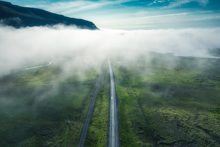 Aerial view of foggy mountain with car driving on the road among mossy wilderness in summer at Icelandの写真素材