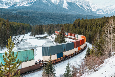 A freight train carrying container passing through the Bow Valley and rocky mountains on winter at Morants Curve, Canadaの写真素材