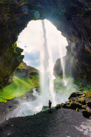 Majestic view of powerful waterfall Kvernufoss flowing and tourist standing in large canyon during...