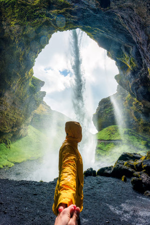 Romantic adventure back view of female tourist in yellow raincoat holding hand inside rocky canyon...