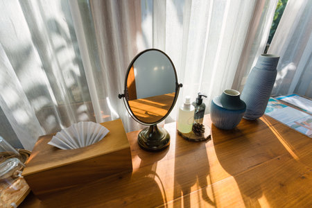 Wooden dressing table with mirror, cream, vase and tissue box by the white curtain window in contemporary tropical resortの写真素材