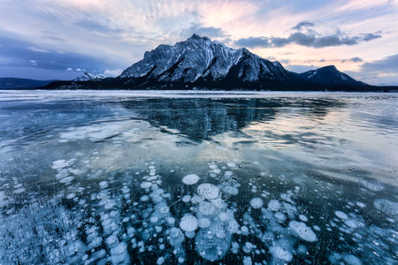 Landscape of natural bubbles frost on frozen Abraham Lake with rocky mountains in winter at Kootenay Plains Area, Alberta, Canadaの写真素材