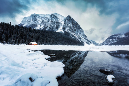 Beautiful scenery of Lake Louise with wooden cottage glowing and rocky mountains with snow covered...