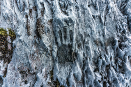 Aged palm hand print on limestone wall in ice cave on winter