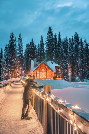 Winter scene of Emerald Lake Lodge glowing over frozen lake with male tourist enjoying in the night...