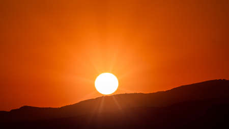 Beautiful and extremely orange sunrise over hillsの写真素材