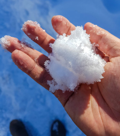 snow in the hands of a child on a background of blue sky