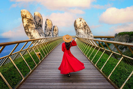Asian woman in Vietnamese national costume on the Golden Bridge with Two Giant Hands, a viewpoint at a popular tourist attraction in Ba Na Hills Resort, Danang, Vietnam.の写真素材