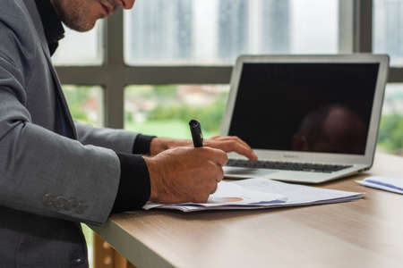 Hand hold pen writing on document, Businessman using computer laptop  working technologyの写真素材