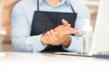 Employee using alcohol gel cleaning hand for working in coffee shopの写真素材