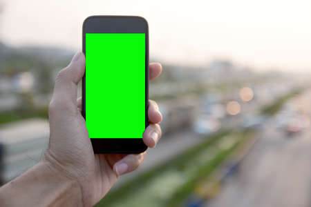Hand holding smartphone against background many car driving on roadの写真素材